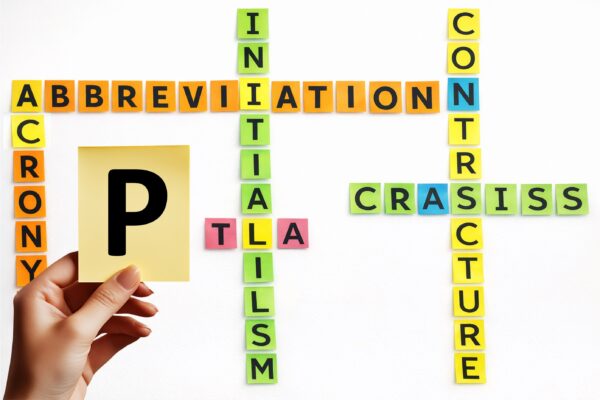 A hand holds a yellow tile with the letter P, surrounded by coloured letter tiles forming medical abbreviations including TLA, arranged in crossword style.