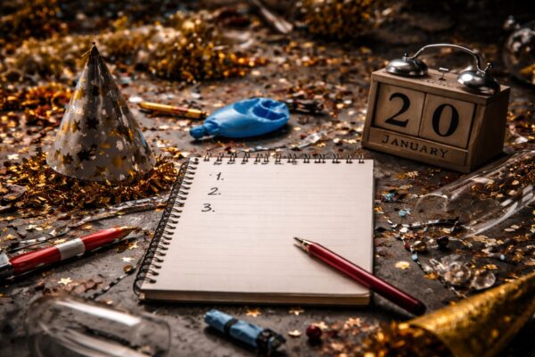 Open notebook with numbered list beside calendar showing 20 January, surrounded by New Year party debris including party hat, confetti and empty bottles.